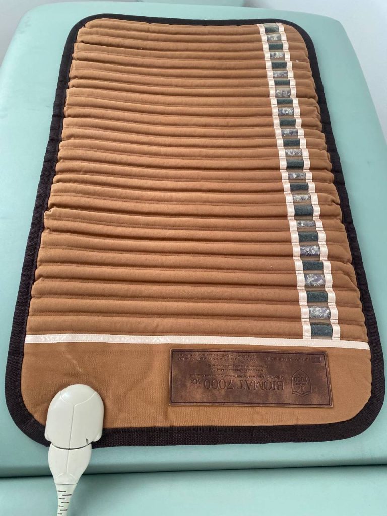 Soft brown mat with a narrow strip containing amethyst and tourmaline with plug and electrical cord attached.